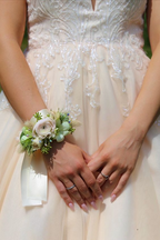 A floral wristlet corsage featuring a large blush-pink ranunculus centered among white dendrobium orchids and delicate spray rose buds. Accented with blue nigella, fluffy bunny tails, and shimmering rhinestone sprays, all tied with a cream-colored satin ribbon