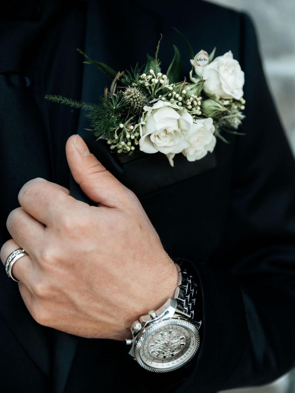 A floral boutonniere styled pocket square featuring cream spray roses, green eryngium thistle, nigella pods, textured seeded eucalyptus, italian ruscus, all bound with a black hand-dyed silk ribbon.