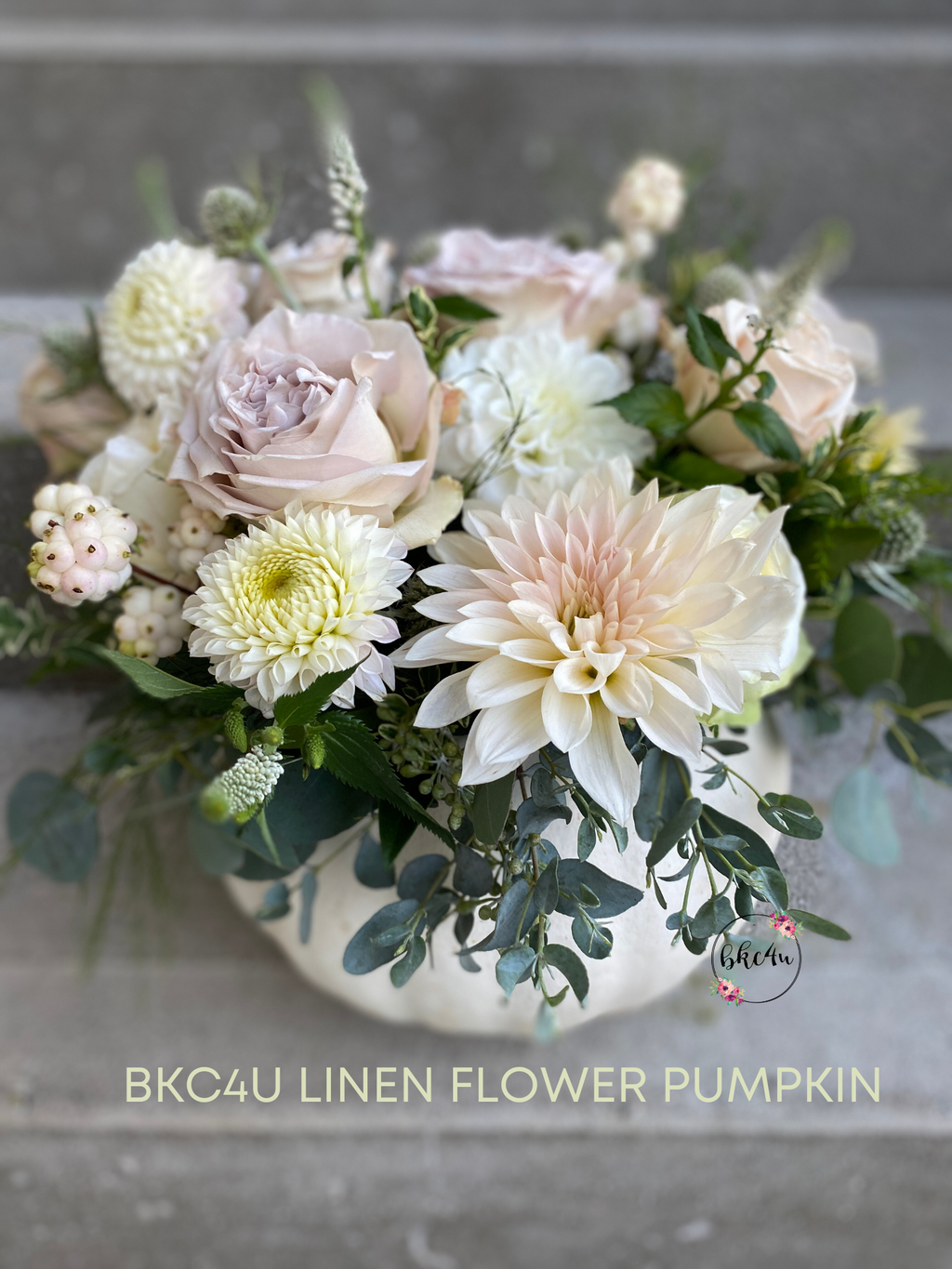 A white pumpkin filled with a mixture of neutral white and pink fresh Dahlias, Roses and greenery.