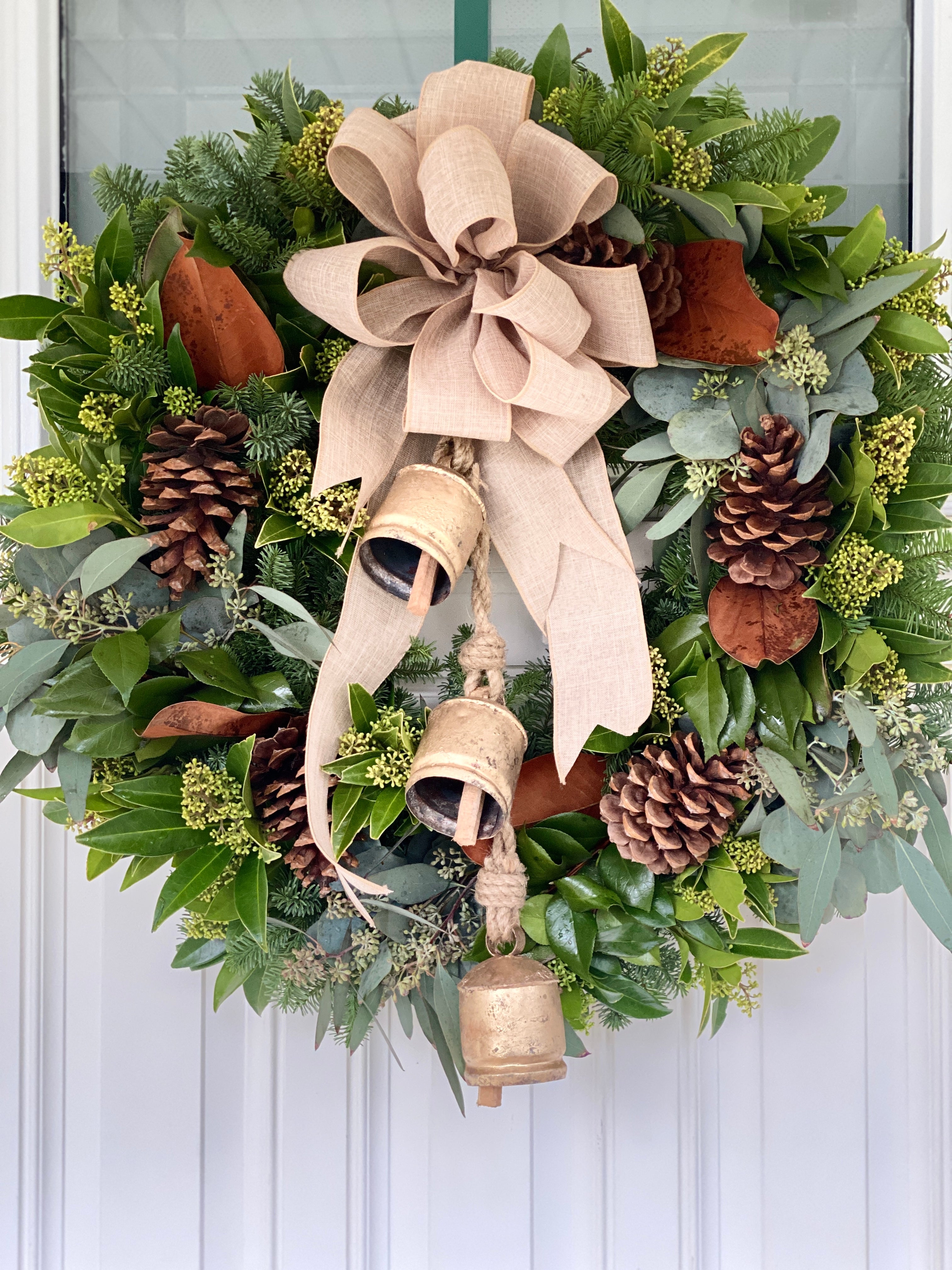 Fresh evergreen boughs create this large festive wreath with a burlap bow and three gold bells hanging from the top.