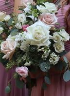Bridesmaid bouquet of white and blush pink roses, pink lisianthus with eucalyptus greenery held by a person in a pink dress.