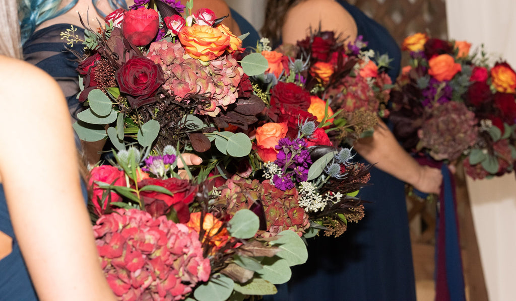 Bridesmaids holding red, orange, and purple, rose, hydrangea, stock, eryngium, moody coloured bouquets for an October wedding.