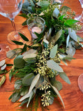Close up of hand woven fresh foliage garland for a table featuring seeded and silver dollar eucalyptus, italian ruscus, plumosa and tree fern varieties.