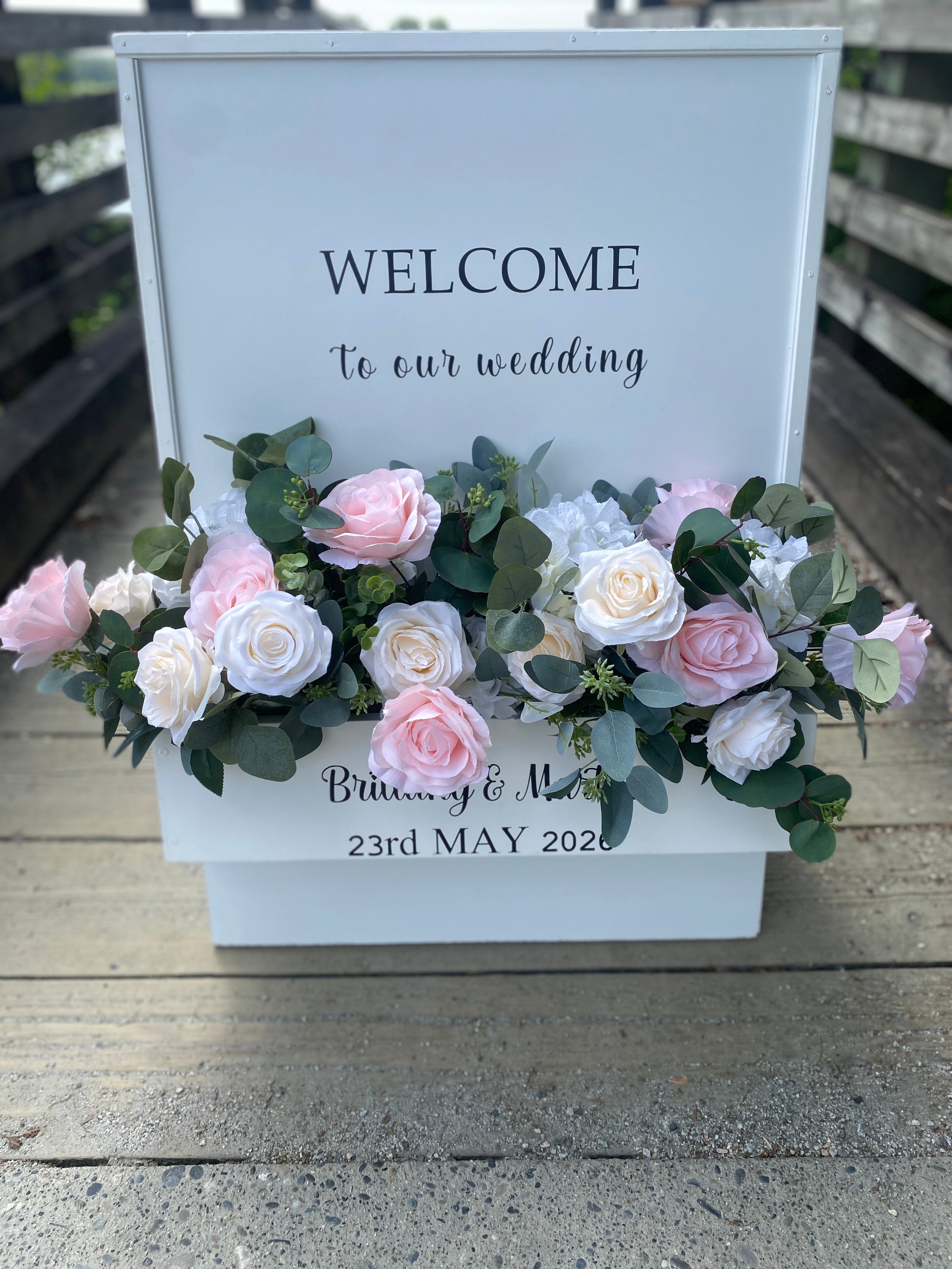 Decorative setup with 'WELCOME' To  Our Wedding" sign, blush and cream rose floral arrangement, at the entrance ramp to the dock viewing the Fraser River in Pitt Meadows.